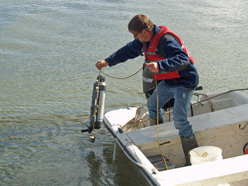 Zac Tait collects a water sample from a skiff tied to the bank.